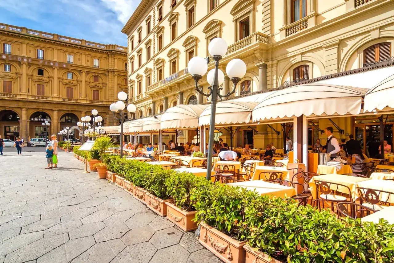 Un caf&eacute; al aire libre en Florencia, perfecto para decidir d&oacute;nde comer en Florencia. Mesas amarillas bajo toldos, gente disfrutando.