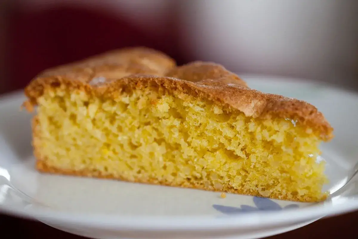 Una fetta di torta soffice e dorata, preparata con farina di mandorle, su un piatto bianco.