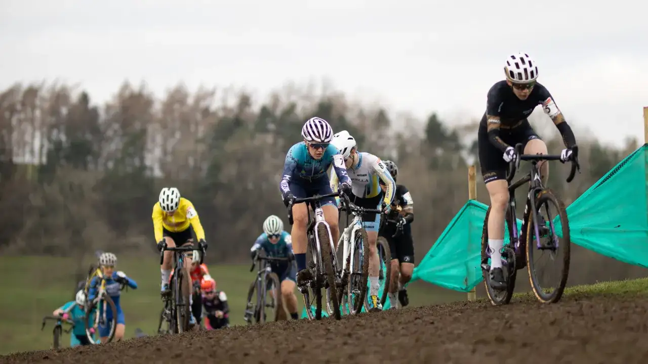 Cyclo cross racers battle through mud and grass, their bikes kicking up dirt.