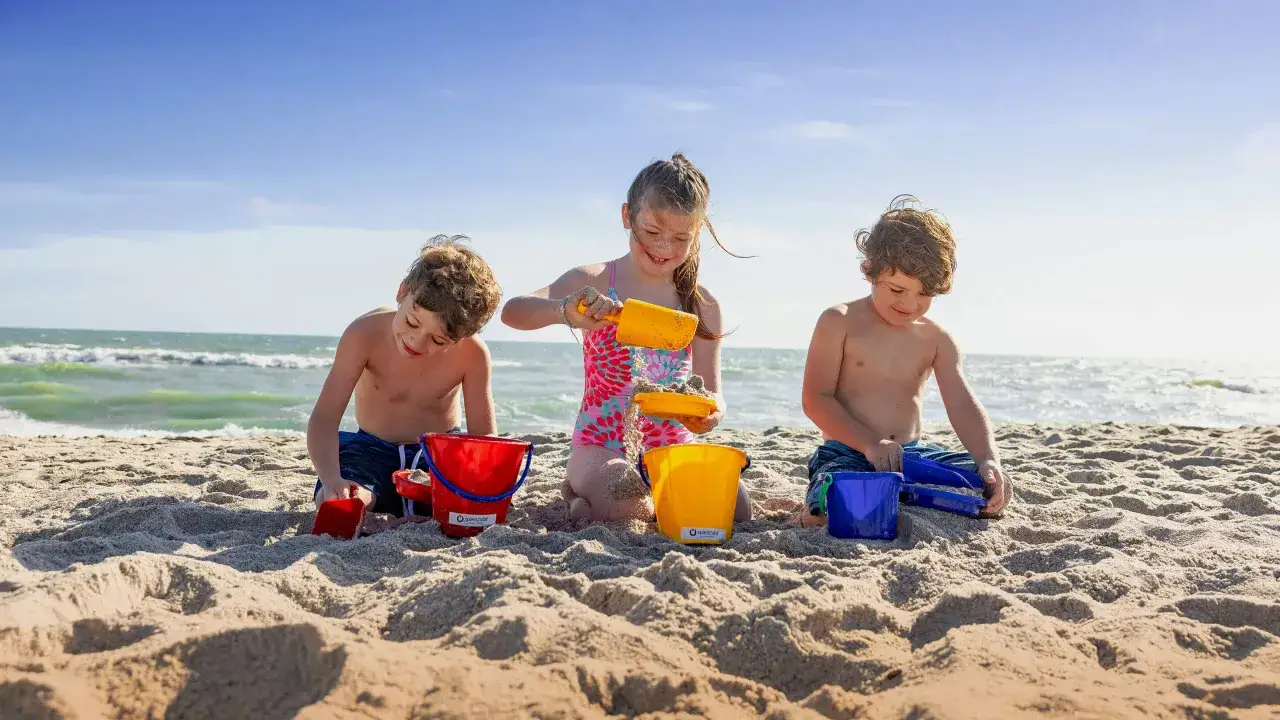 Tr&oacute;jka dzieci świetnie się bawi na plaży, budując zamki z piasku. Radość i beztroska zabawy na piasku.