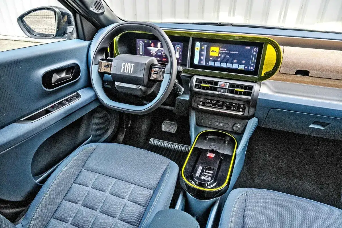 Wnętrze nowego Fiata Pandiny z niebieskimi siedzeniami i deską rozdzielczą. Kierownica z logo FIAT, cyfrowe ekrany i nowoczesny panel środkowy.
