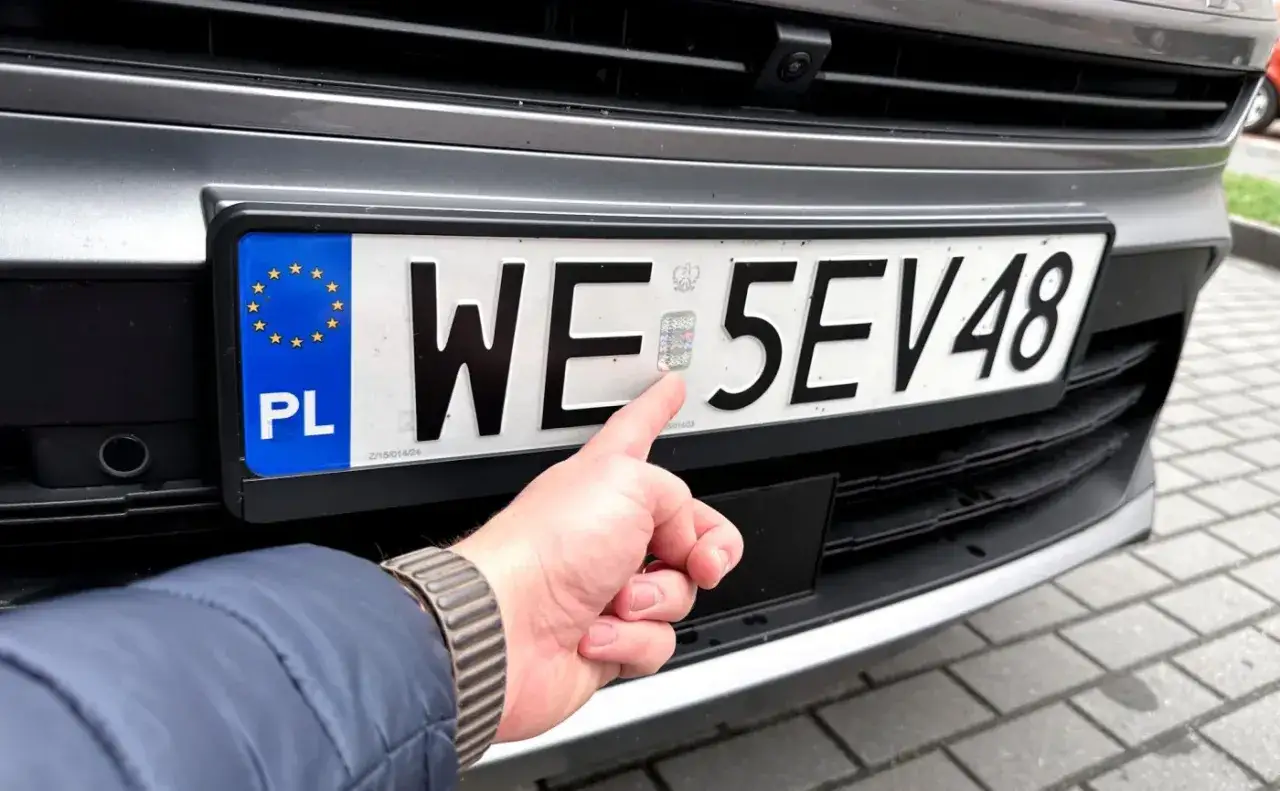 Palec wskazuje hologram na tablicy rejestracyjnej. Młody kierowca sprawdza autentyczność dokumentów.