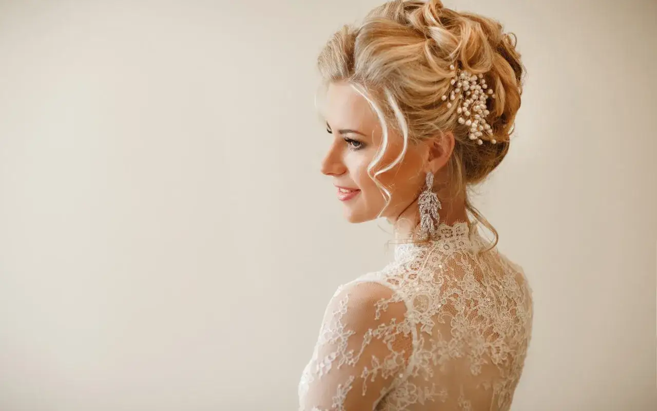 Elegancka panna młoda z upiętymi włosami ozdobionymi perłami i kryształami. Jej fryzury ślubne glamour podkreślają delikatne loki opadające na ramiona.