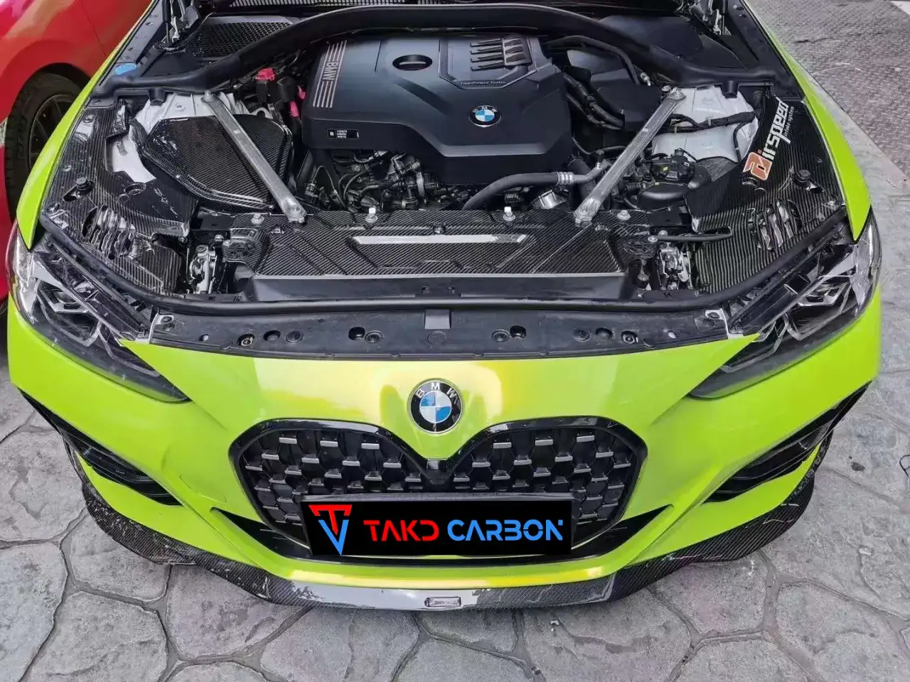 Jasnozielone BMW z otwartą maską, widoczny silnik i elementy z włókna węglowego. Logo TAKO CARBON na grillu. Model b48.