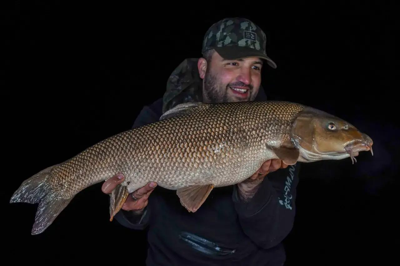 Un pêcheur souriant tient une belle loche d'étang aux écailles dorées, fièrement exhibée dans la nuit.