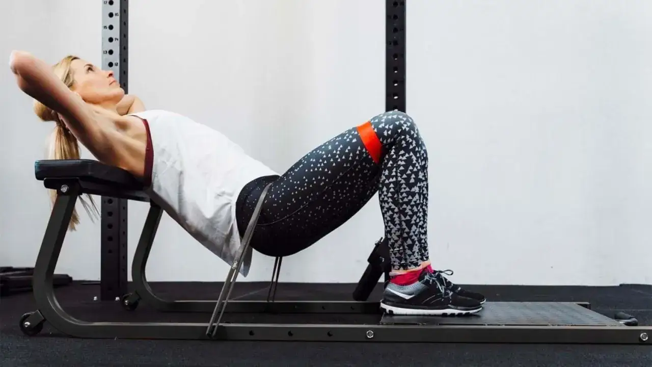 Kobieta wykonuje ćwiczenie hip thrust w domu, używając taśmy oporowej na udach.