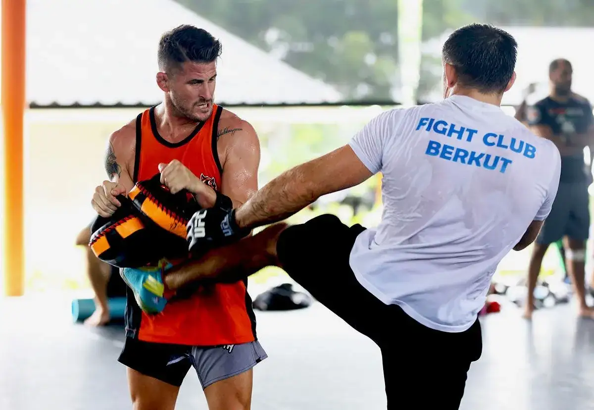 Trainer demonstrates how to hold pads for boxing, as a fighter practices kicks.