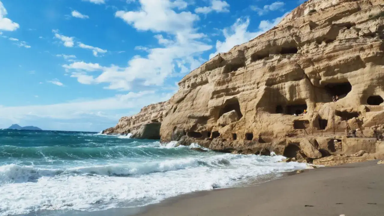 Plaża Matala z falami rozbijającymi się o brzeg i skalnymi jaskiniami w zboczu.