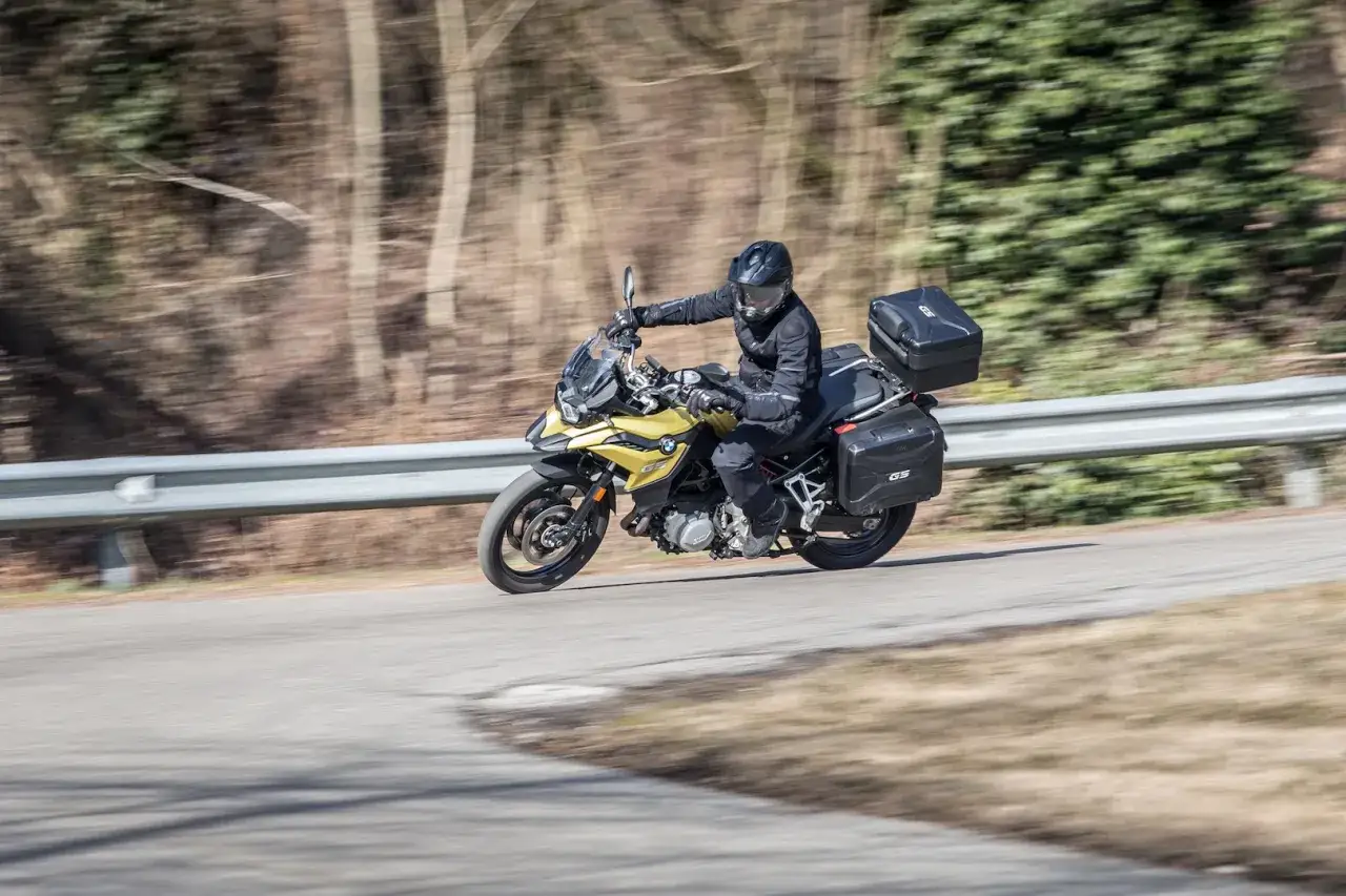Motociclista su moto da turismo gialla con borse laterali e bauletto, in movimento su strada. La differenza tra moto e scooter &egrave; evidente nella posizione di guida e nel design.