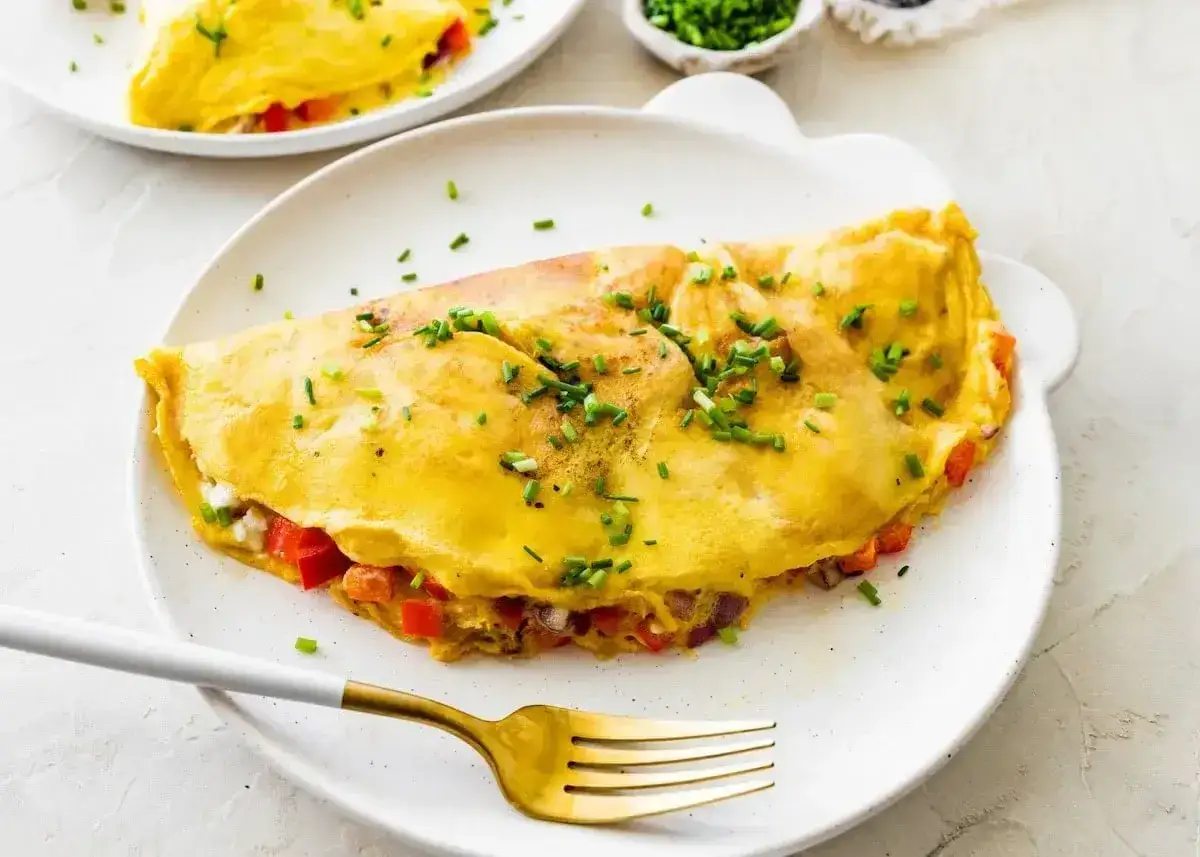 Puszysty omlet z białek z warzywami, posypany szczypiorkiem, czeka na złoty widelec.