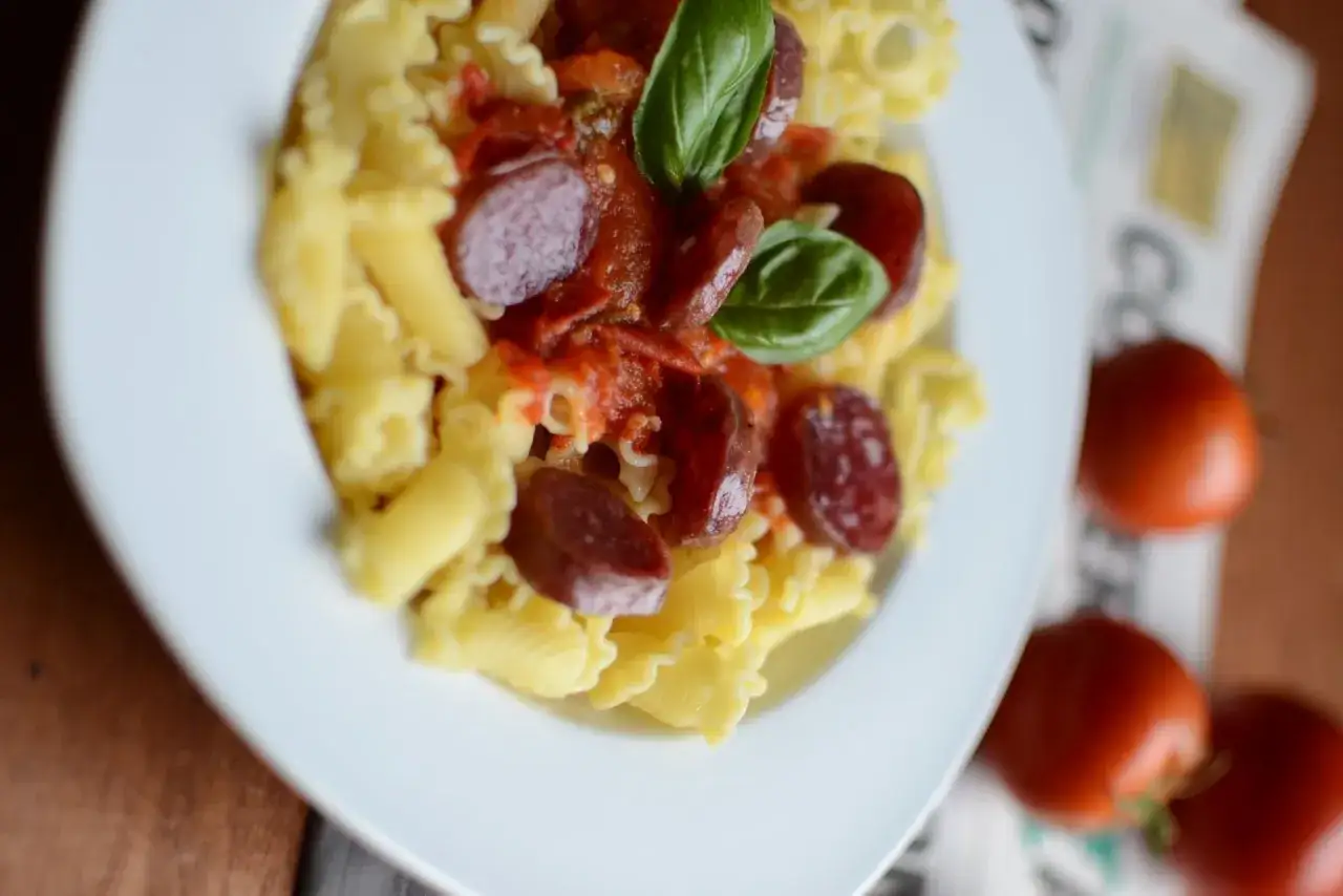 Pâtes pici all'aglione avec des rondelles de saucisse, sauce tomate et basilic frais. Un plat savoureux et coloré.