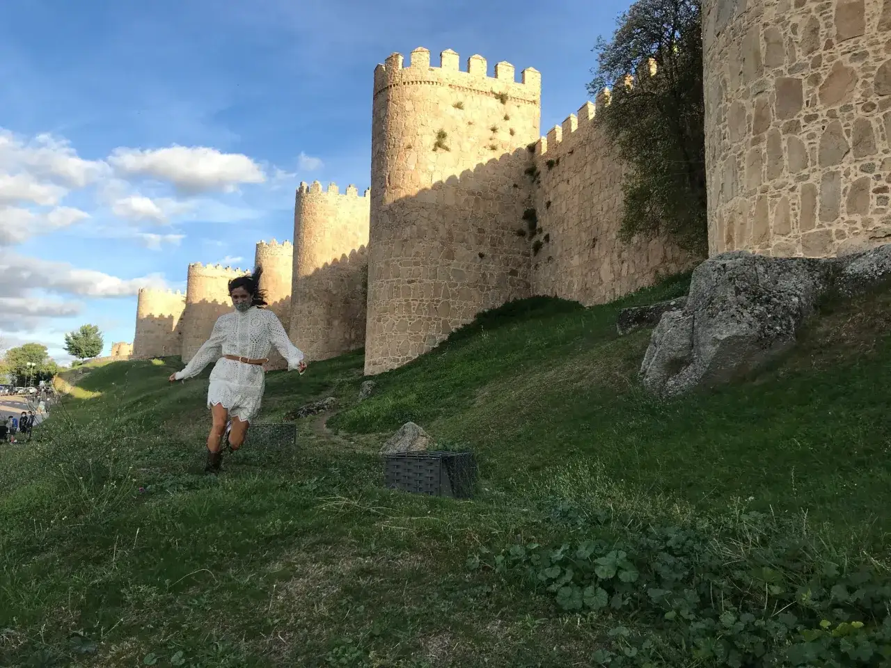 Una mujer corre por la hierba frente a las murallas de Ávila. Parece que está jugando con niños invisibles.