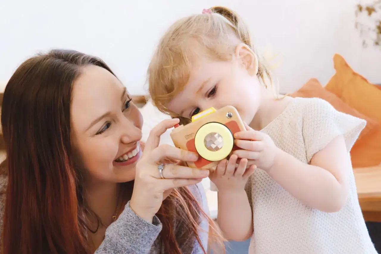 Mamma e figlia giocano con una macchinetta fotografica di legno. Un momento di gioia che dimostra come i bambini vogliano sempre giocare con la mamma.