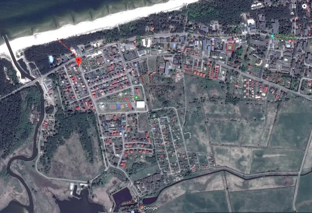 Widok satelitarny Dźwirzyna z zaznaczonymi noclegami blisko morza. Widać zabudowania, plażę i fragment wybrzeża.