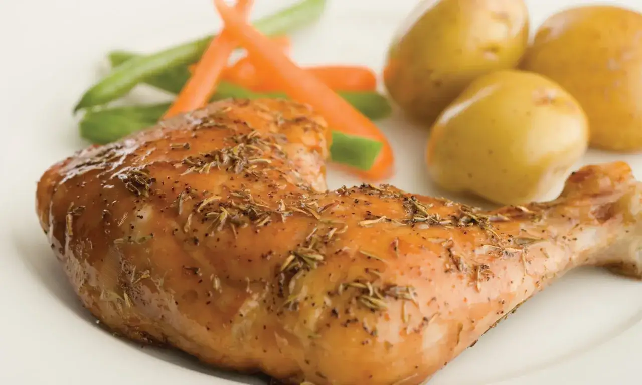 Un délicieux haut de cuisse de poulet rôti, assaisonné d'herbes, servi avec des pommes de terre et des légumes verts.