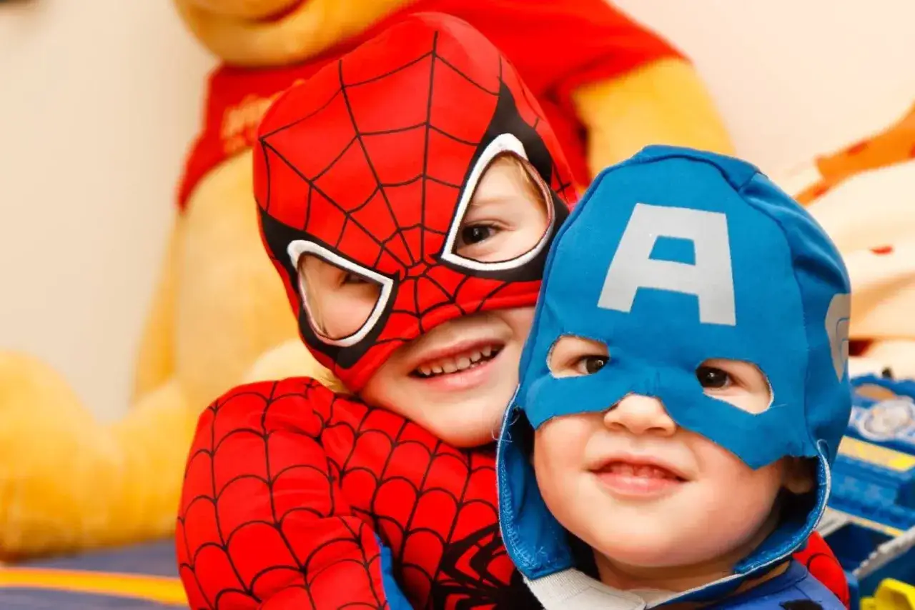 Dw&oacute;ch chłopc&oacute;w w strojach superbohater&oacute;w, jeden jako Spider-Man, drugi jako Kapitan Ameryka, cieszy się zabawą w odgrywanie r&oacute;l.