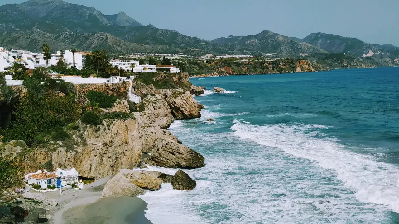 Acantilados blancos y mar turquesa en la mejor playa de Nerja. Una casita blanca con techo azul descansa en la arena.