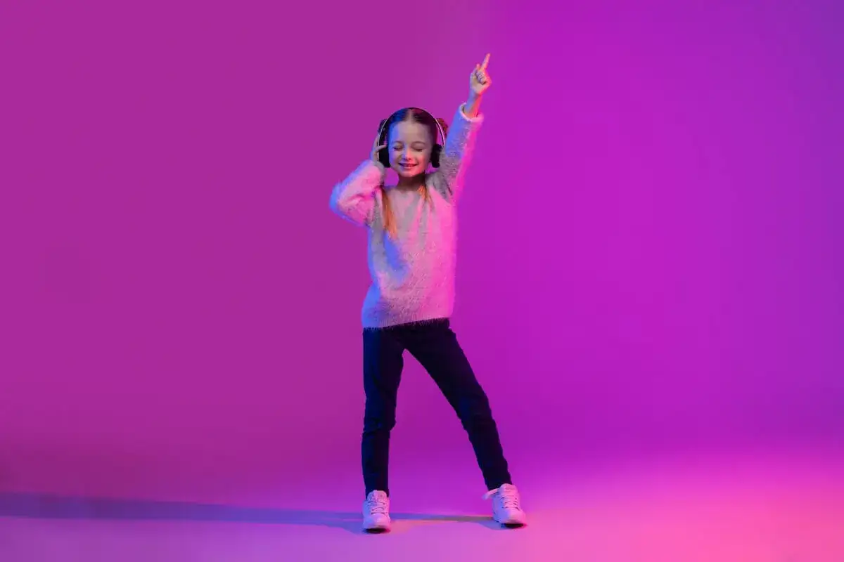 Ni&ntilde;a con auriculares baila feliz, con un dedo apuntando al cielo. &iexcl;Pura alegr&iacute;a de bailar ni&ntilde;os!