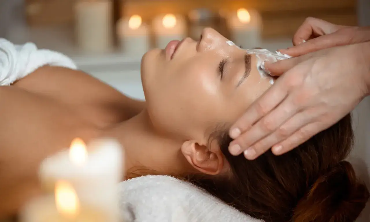 Trattamento viso con crema, un massaggio rilassante per contrastare il viso cadente. Candele accese creano un'atmosfera serena.