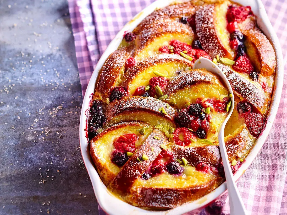 Un délicieux pain perdu aux fruits rouges et pistaches, saupoudré de sucre glace, servi dans un plat blanc.