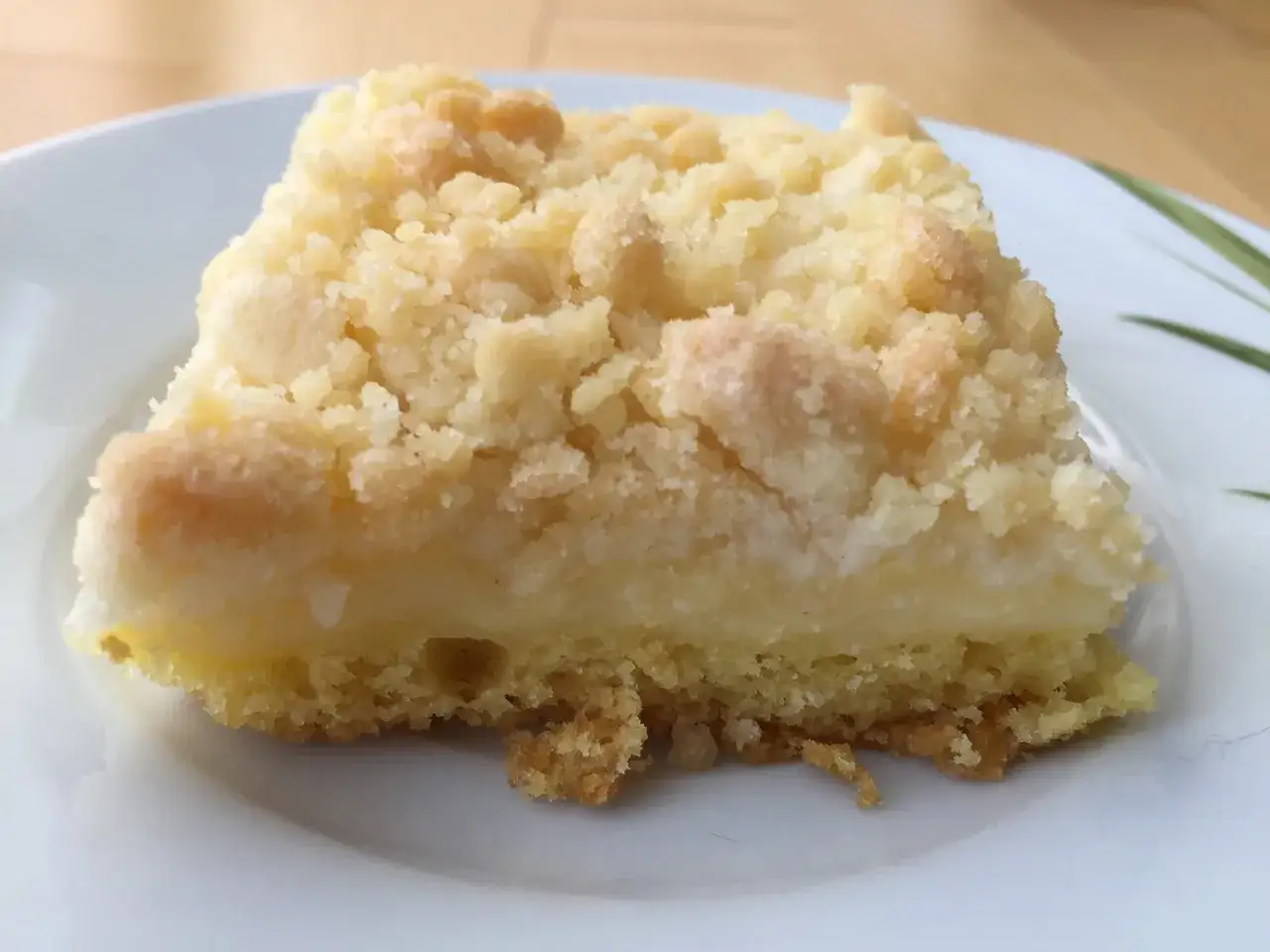Ein St&uuml;ck Puddingstreuselkuchen auf einem Teller. Der Kuchen hat eine cremige Puddingf&uuml;llung und eine knusprige Streuseldecke.