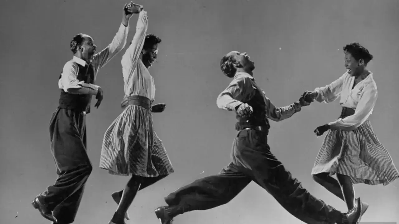 Coppia di ballerini in pieno lindy hop, con movimenti energici e gioiosi.