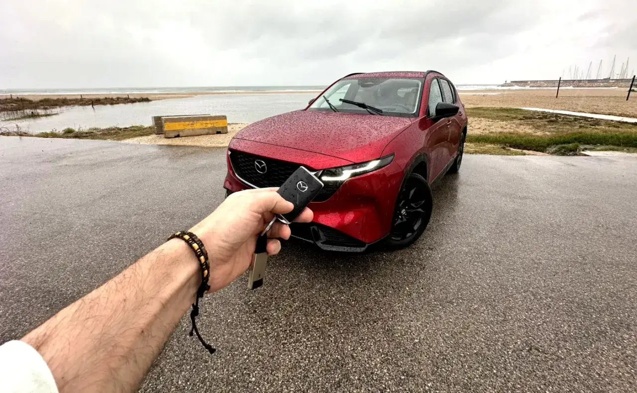 Czerwony suv Mazda CX-5 na mokrym parkingu nad morzem. Kluczyk w dłoni gotowy do otwarcia.