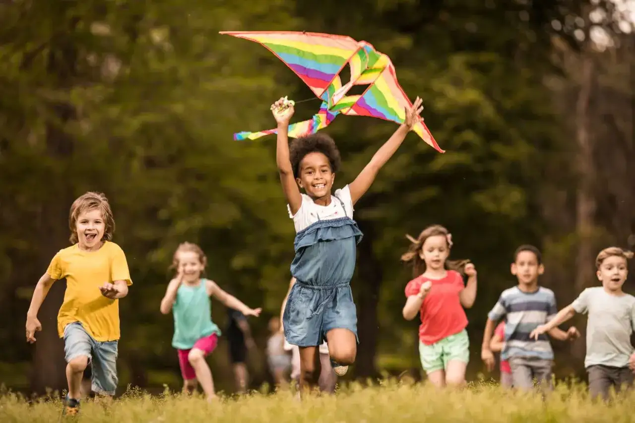 Kinder rennen lachend mit einem bunten Lenkdrachen im Gras. Warum sind Kinder so laut? Weil sie das Leben in vollen Zügen genießen!