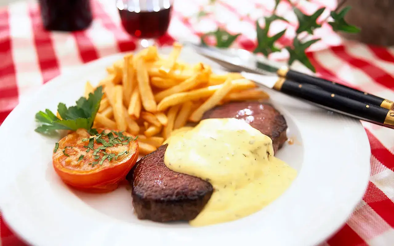 En klassisk steak frites med pommes frites, en halverad tomat och en krämig sås.