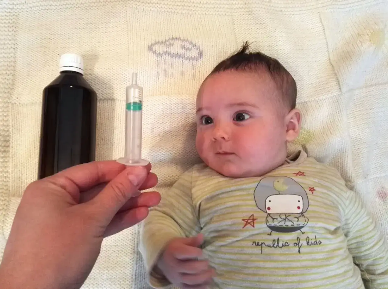 Bebé de 1 mes con resfriado, listo para su medicina. Una mano sostiene una jeringa con líquido.