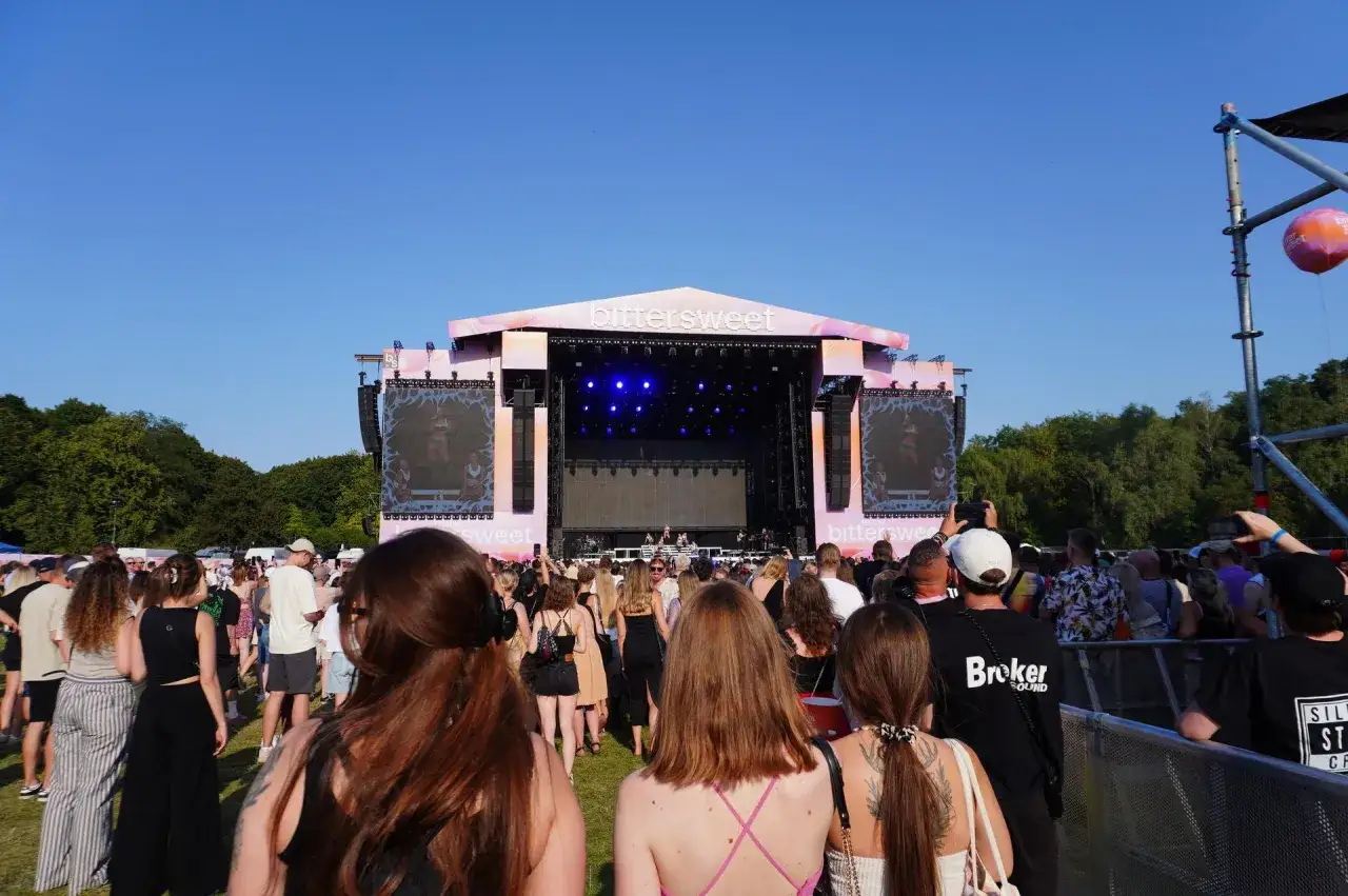 Tłum ludzi na festiwalu Bittersweet 2026, patrzący na scenę z wielkim ekranem. Słońce świeci, tworząc radosną atmosferę.