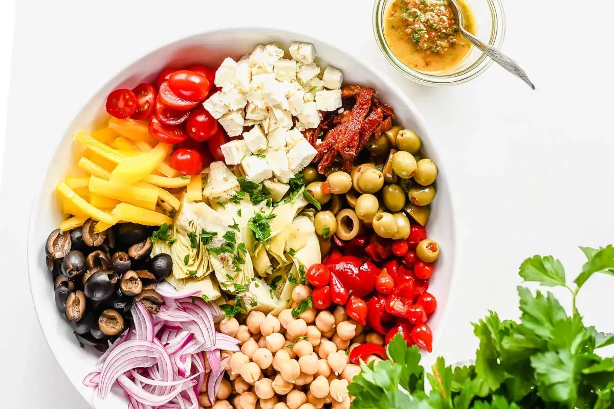 Salade color&eacute;e avec des c&oelig;urs d'artichaut, des tomates cerises, des poivrons jaunes, des olives noires et vertes, des pois chiches, des oignons rouges, du fromage feta et des poivrons rouges.