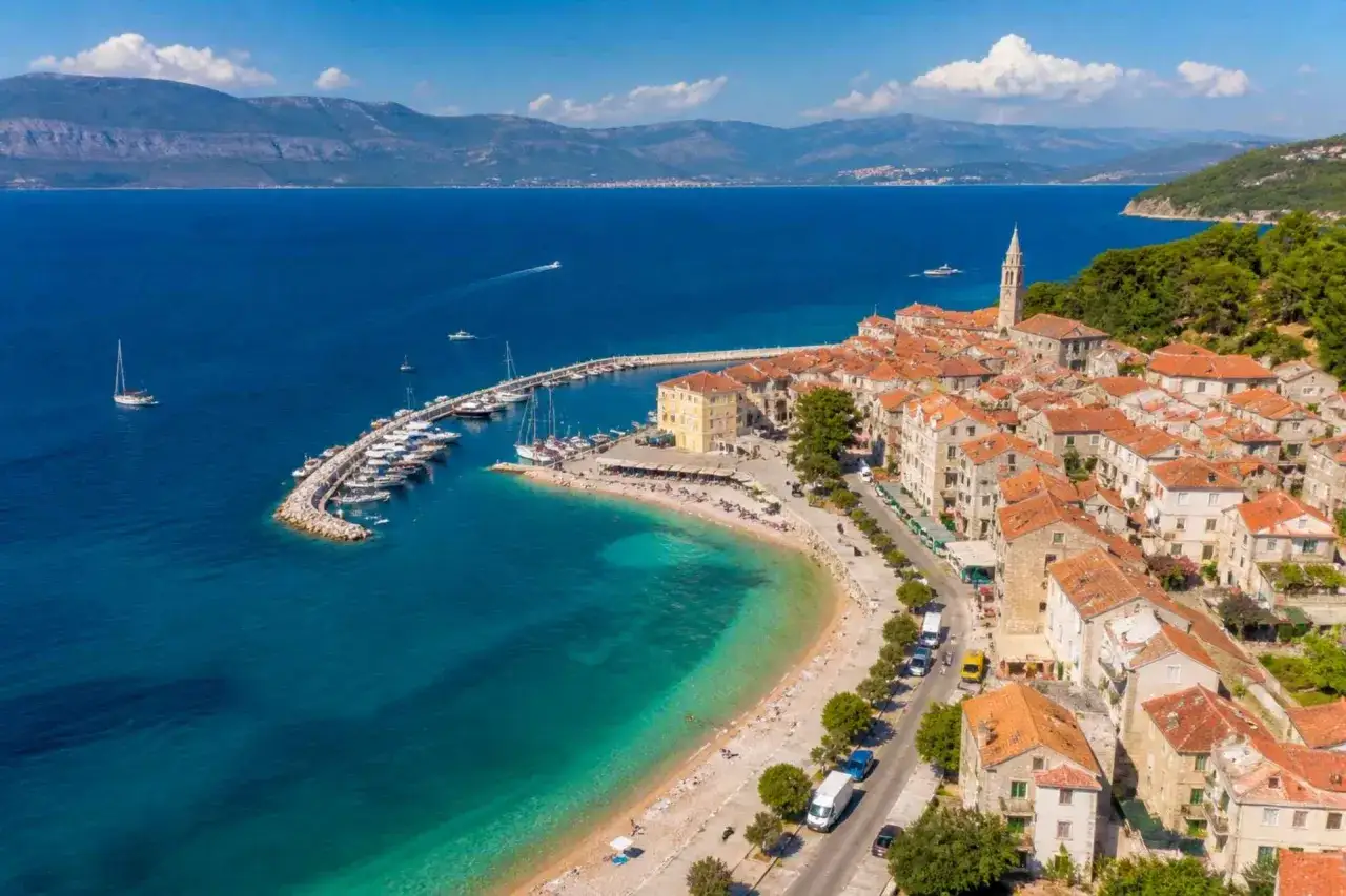 Malownicze miasteczko na wyspie Brač z portem pełnym łodzi, plażą i kamiennymi domami pod czerwonymi dachami.