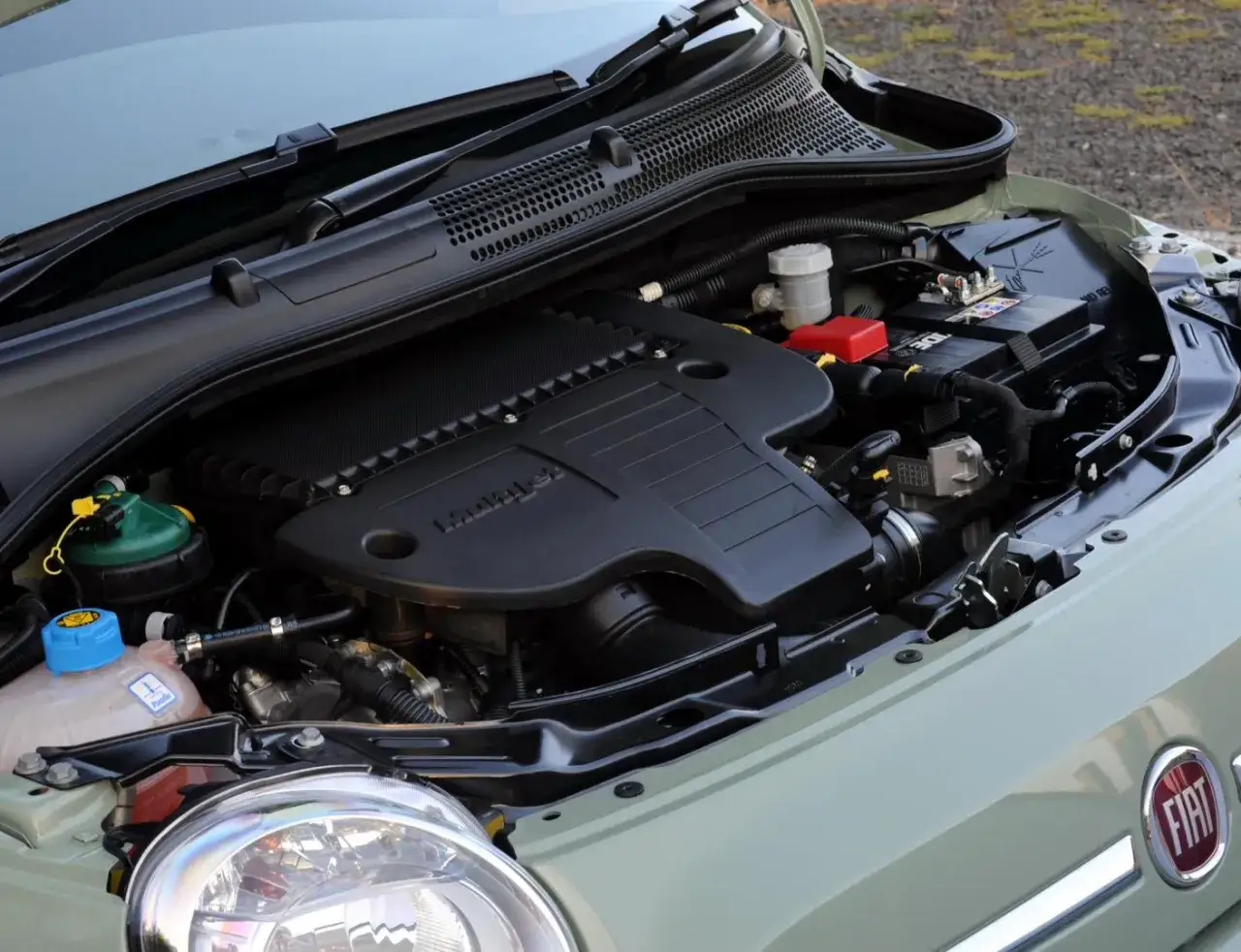 Silnik 1.3 Multijet w samochodzie Fiat. Widoczny akumulator, płyny i elementy osprzętu.