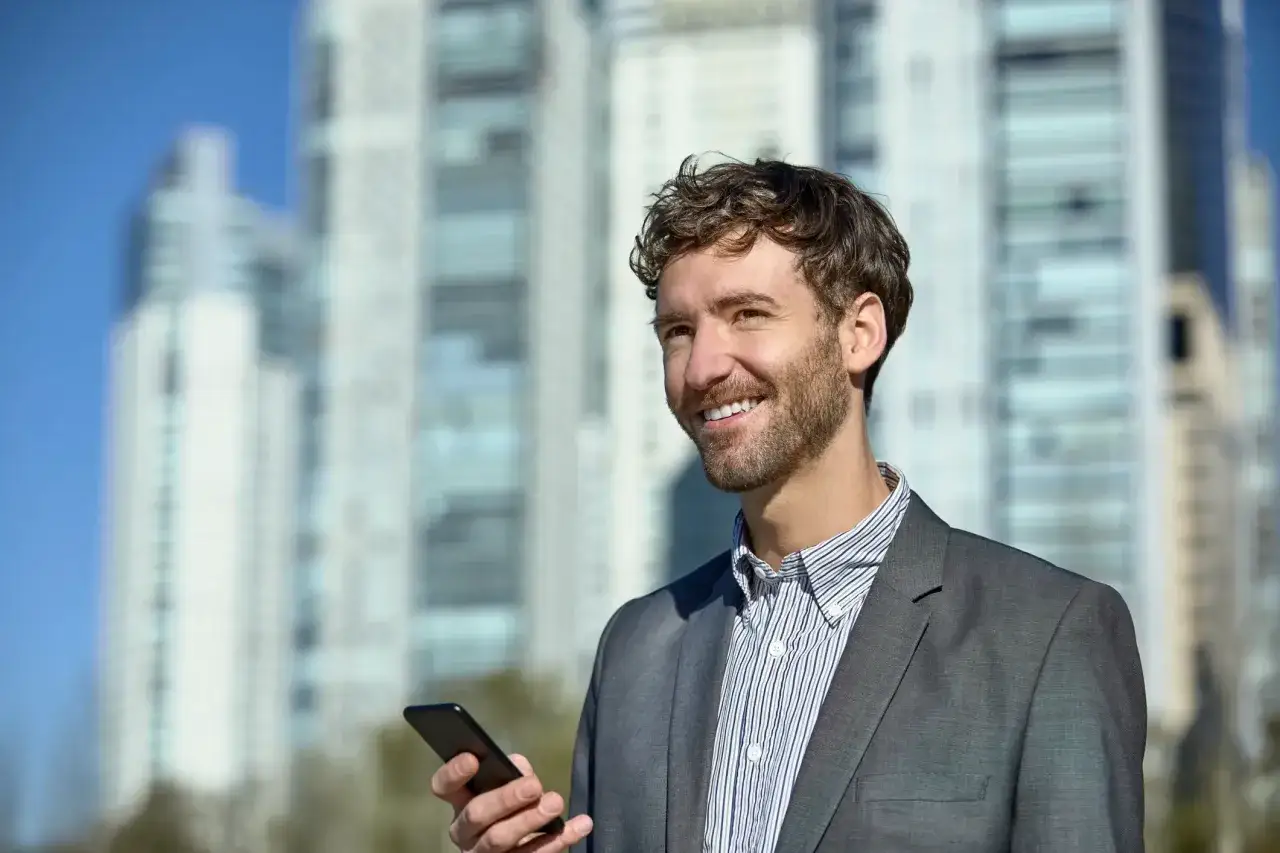 Man med mobiltelefon framför skyskrapor. Han ler och verkar nöjd med sin utbildning inom fastighet.