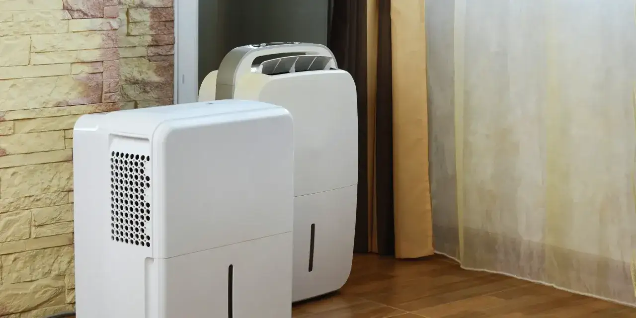 Dwa białe osuszacze powietrza stoją obok siebie, gotowe do działania. To prosty sposób, jak osuszyć ściany domowym sposobem, zapobiegając wilgoci.