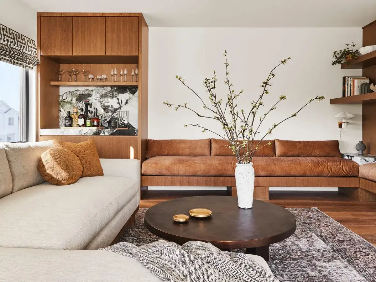 Sof&aacute; beige y marr&oacute;n, mesa de caf&eacute;, alfombra, estanter&iacute;as con bebidas y decoraci&oacute;n, todo en un espacio acogedor que evita el ruido visual.