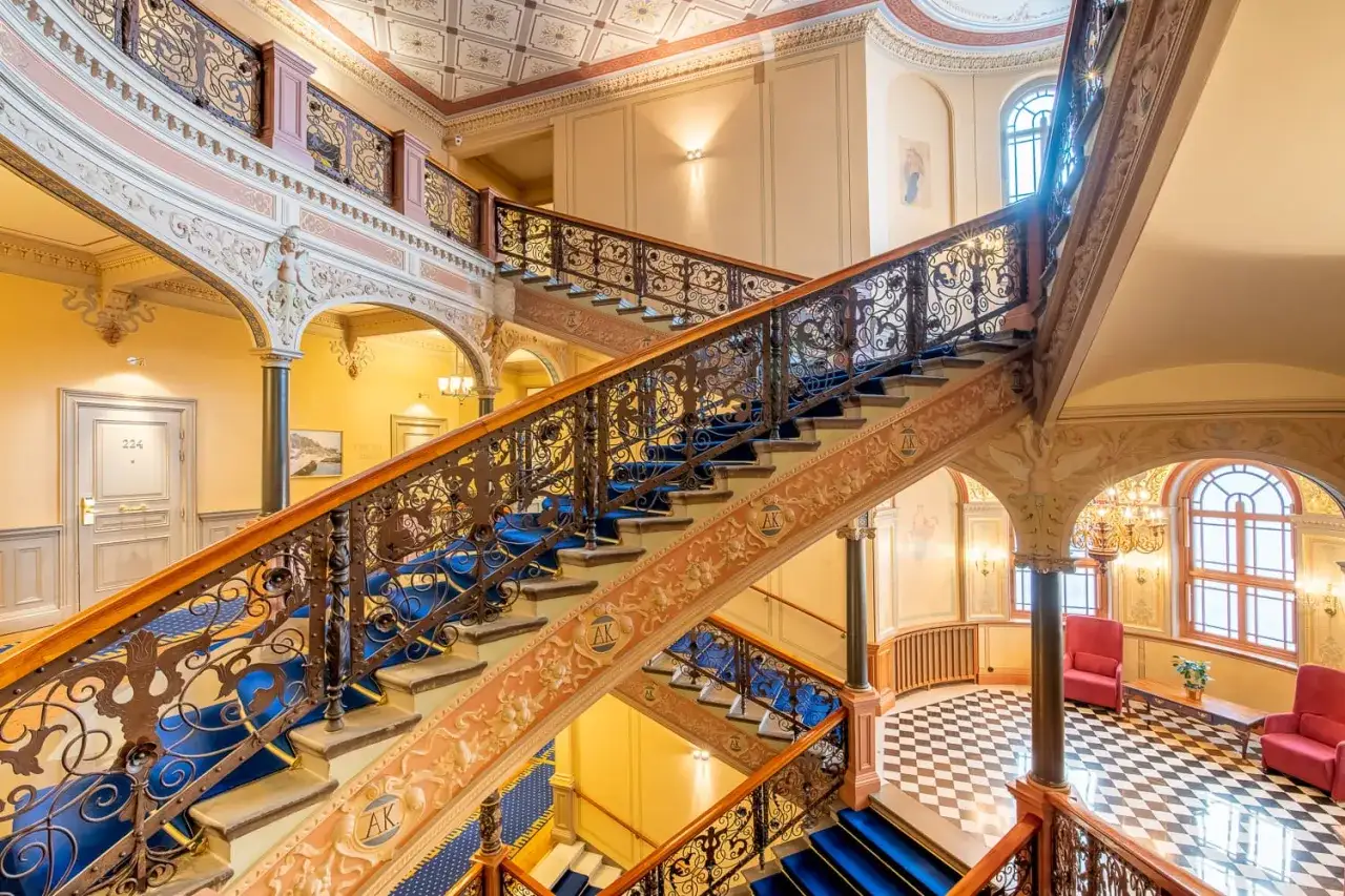 En storslagen trappa med bl&aring; helt&auml;ckningsmatta och utsmyckade r&auml;cken. En p&aring;minnelse om hotell Knausts historia och dess eleganta arkitektur.