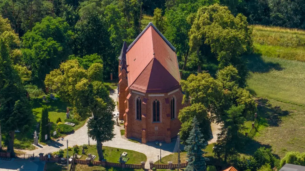 Kościół w Dębnie otoczony zielenią, z cmentarzem i krzyżami.