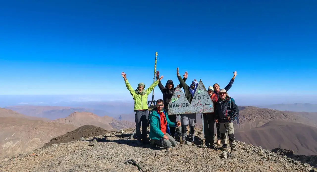 Groupe de randonneurs victorieux au sommet du mont M'Goun, 4071m. Le ciel est d'un bleu &eacute;clatant, les montagnes s'&eacute;tendent &agrave; perte de vue.
