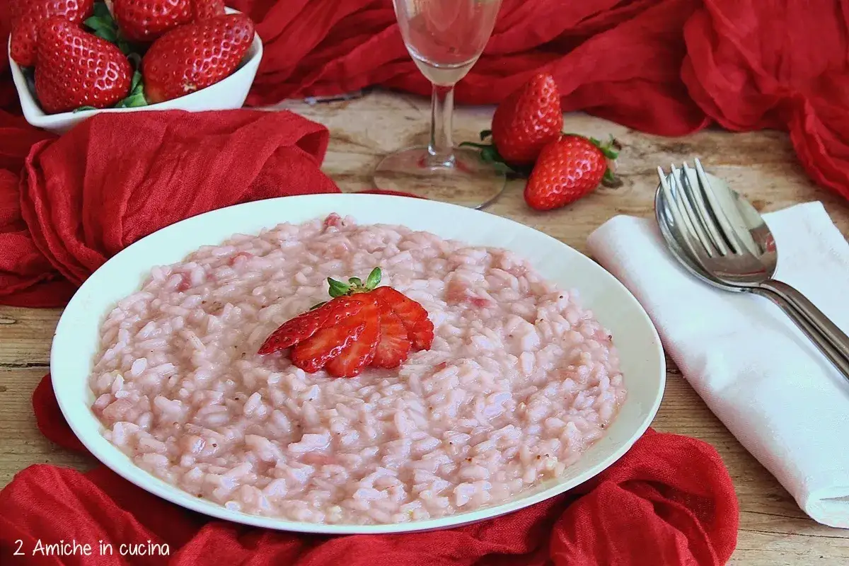 Un cremoso risotto alle fragole, guarnito con una fragola fresca, su un piatto bianco, con fragole e tessuto rosso sullo sfondo.