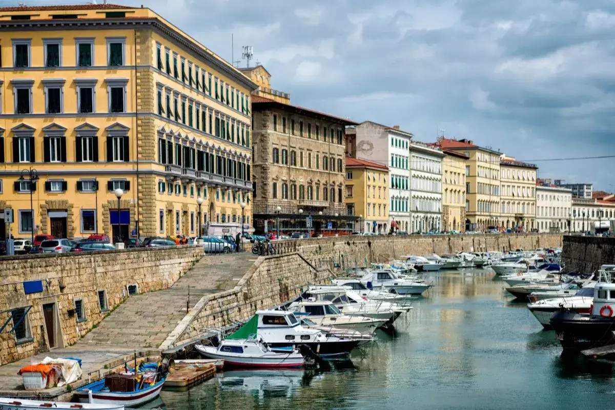 Edifici storici e barche ormeggiate lungo il canale del terminal crociere Livorno, con un cielo nuvoloso.