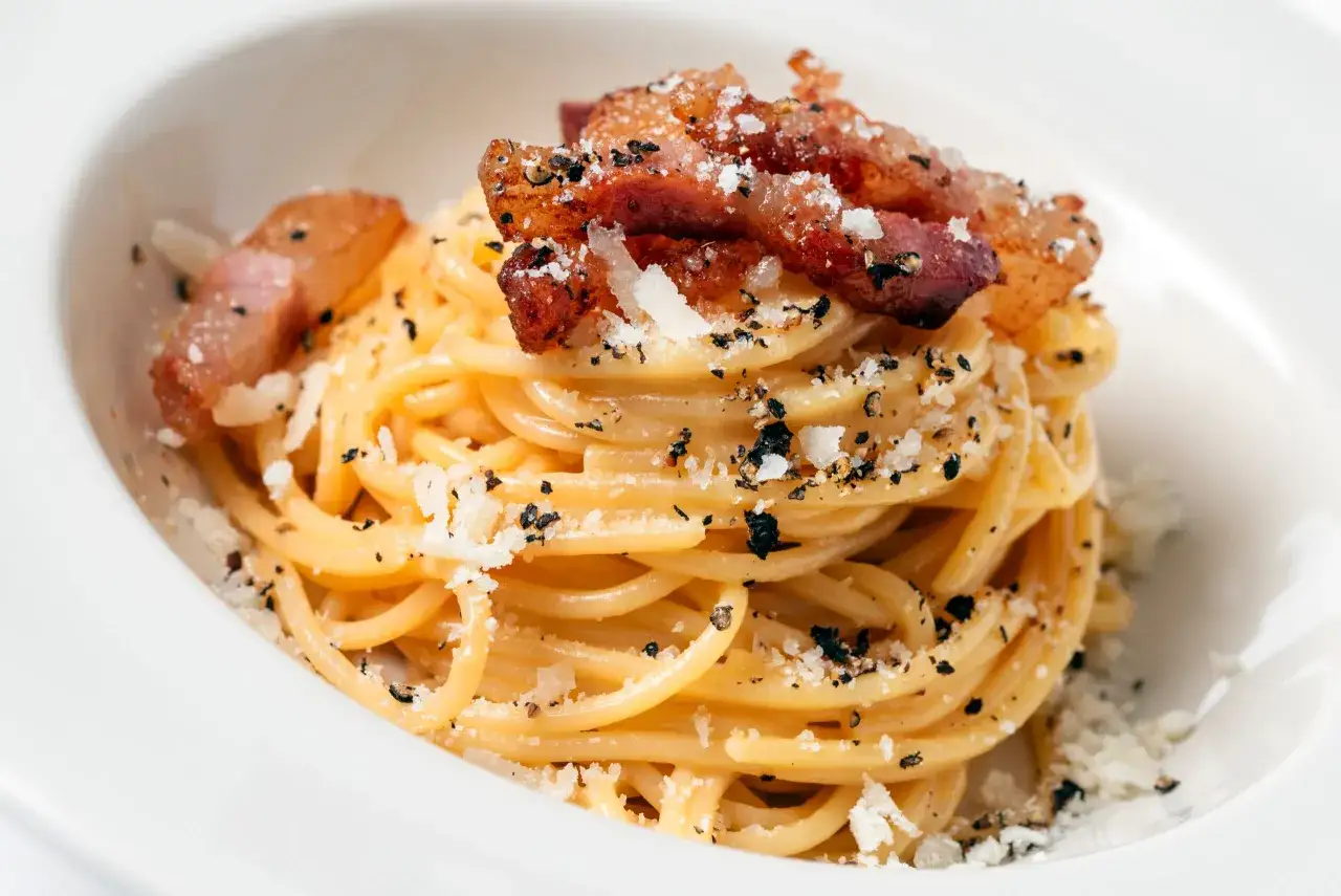 Pyszne spaghetti carbonara z chrupiącym guanciale, posypane parmezanem i czarnym pieprzem.
