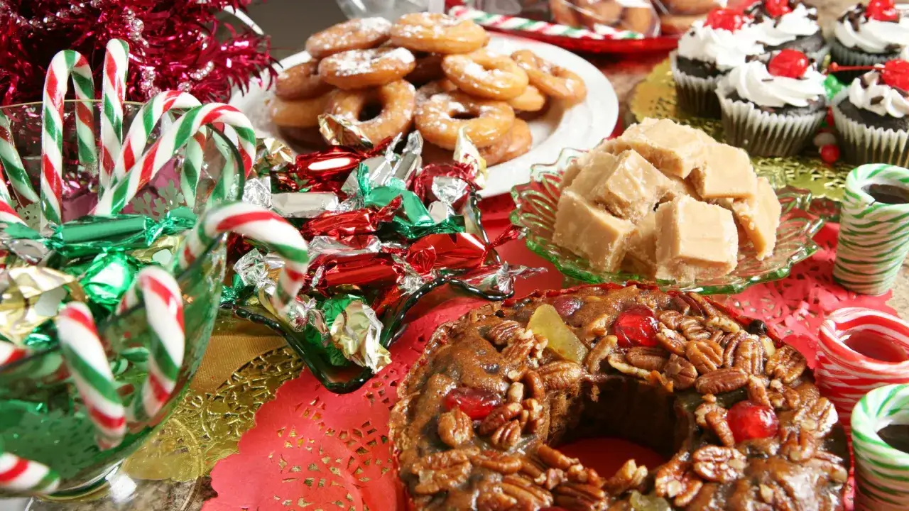 Una mesa llena de deliciosos postres navide&ntilde;os: pastel de frutas, fudge, donas, cupcakes y bastones de caramelo.