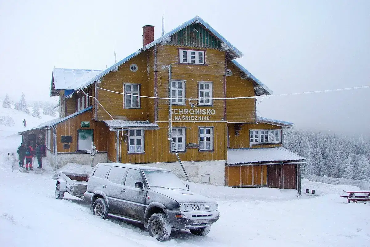 Sch<bos>isko na Śnieżniku, żółty budynek w śniegu, gdzie jest śnieżnik. Samochód z przyczepą na tle zimowego krajobrazu.