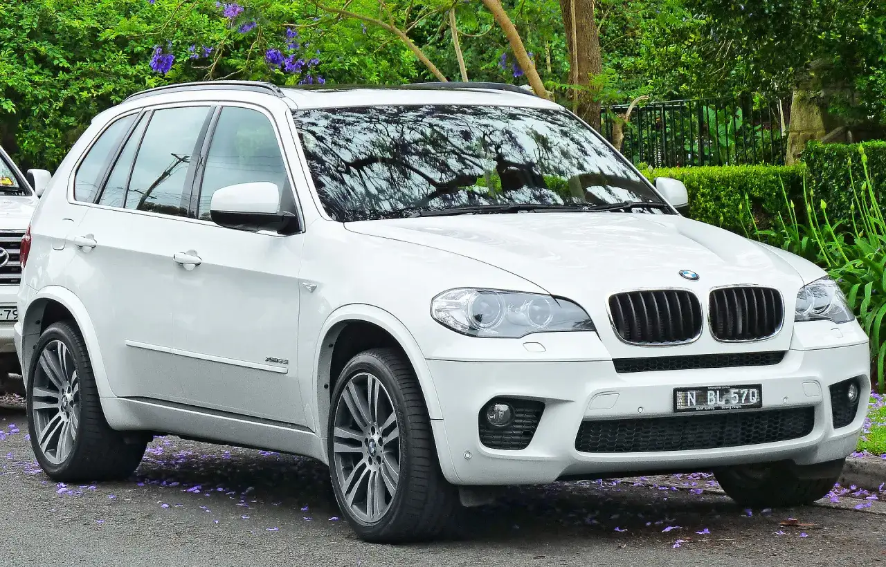 Białe BMW X5 na tle zieleni. Wiele osób szuka bmw x5 opinie, by podjąć decyzję o zakupie.