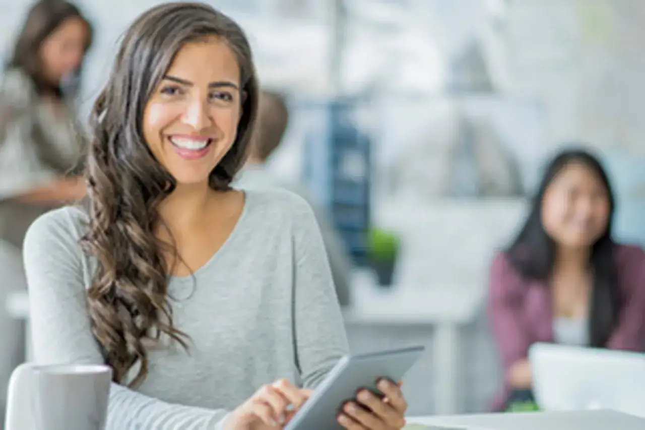 Mujer sonríe mientras usa una tableta, preparándose para trabajar en Canadá.