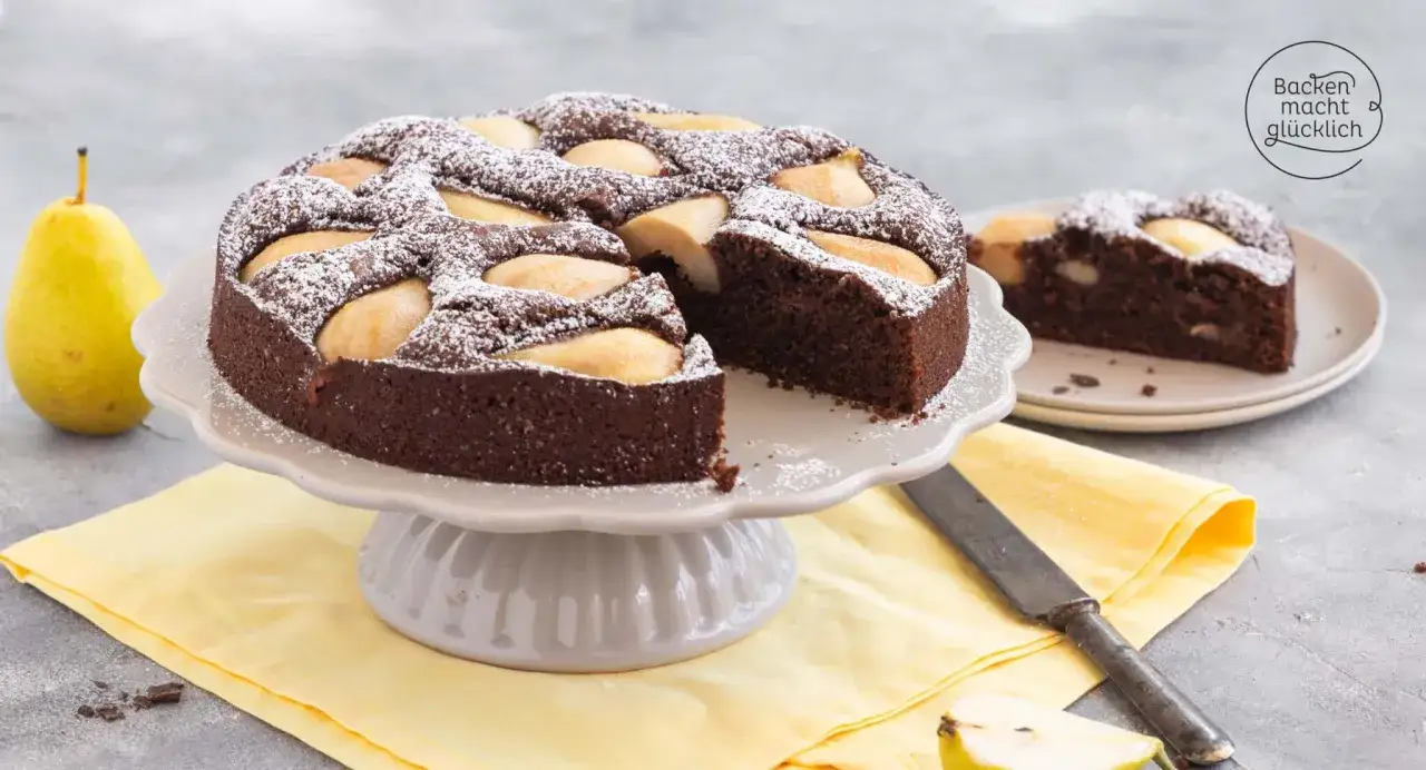 Saftiger birnen schoko kuchen, mit Puderzucker best&auml;ubt, auf einem Kuchenst&auml;nder. Daneben ein St&uuml;ck Kuchen auf einem Teller.