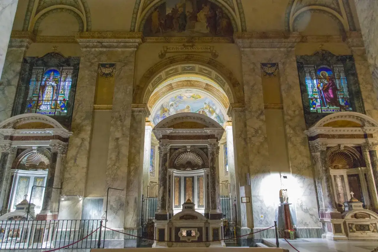 Interior of a church in Tre Fontane, Rome, featuring stained glass windows, marble columns, and a central altar.