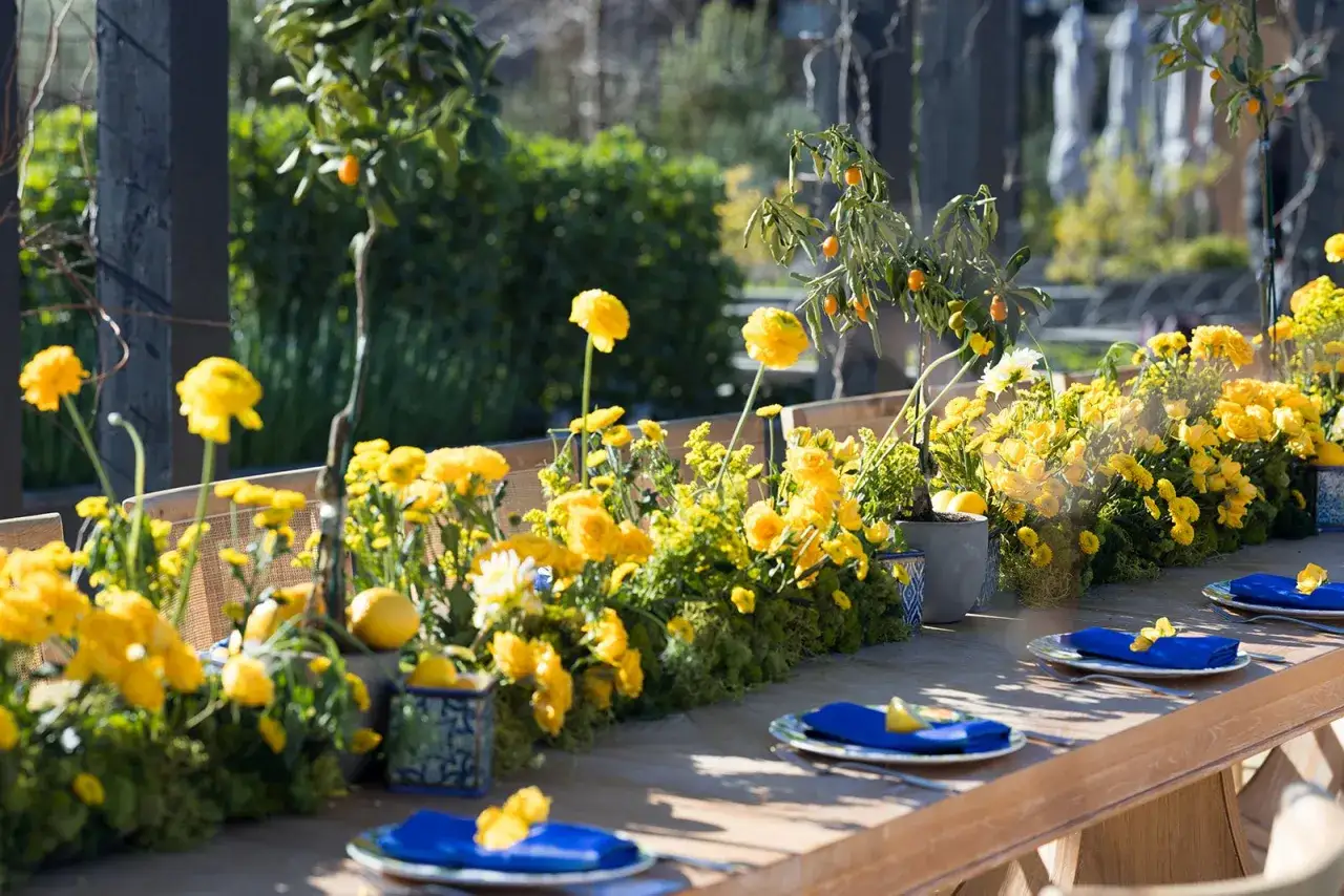 Une table dressée pour un repas en plein air, ornée d'une abondance de fleurs jaunes vives et de kumquats. Une deco table nature chic qui invite à la détente.